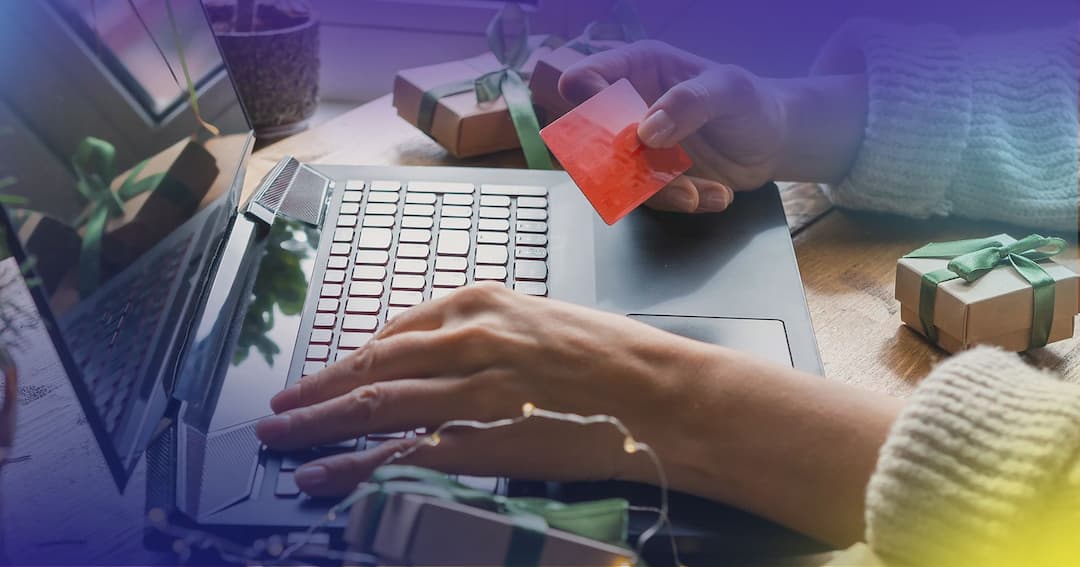 Woman's hands holding credit card while on laptop with presents around.