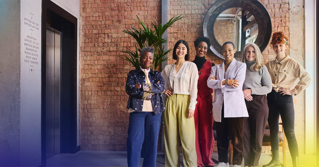 Six diverse women in business clothes standing against the wall.